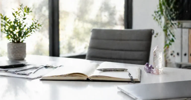Bureau épuré avec cahier ouvert, stylo, plante verte et cristaux symbolisant le cadre professionnel et éthique des soins énergétiques