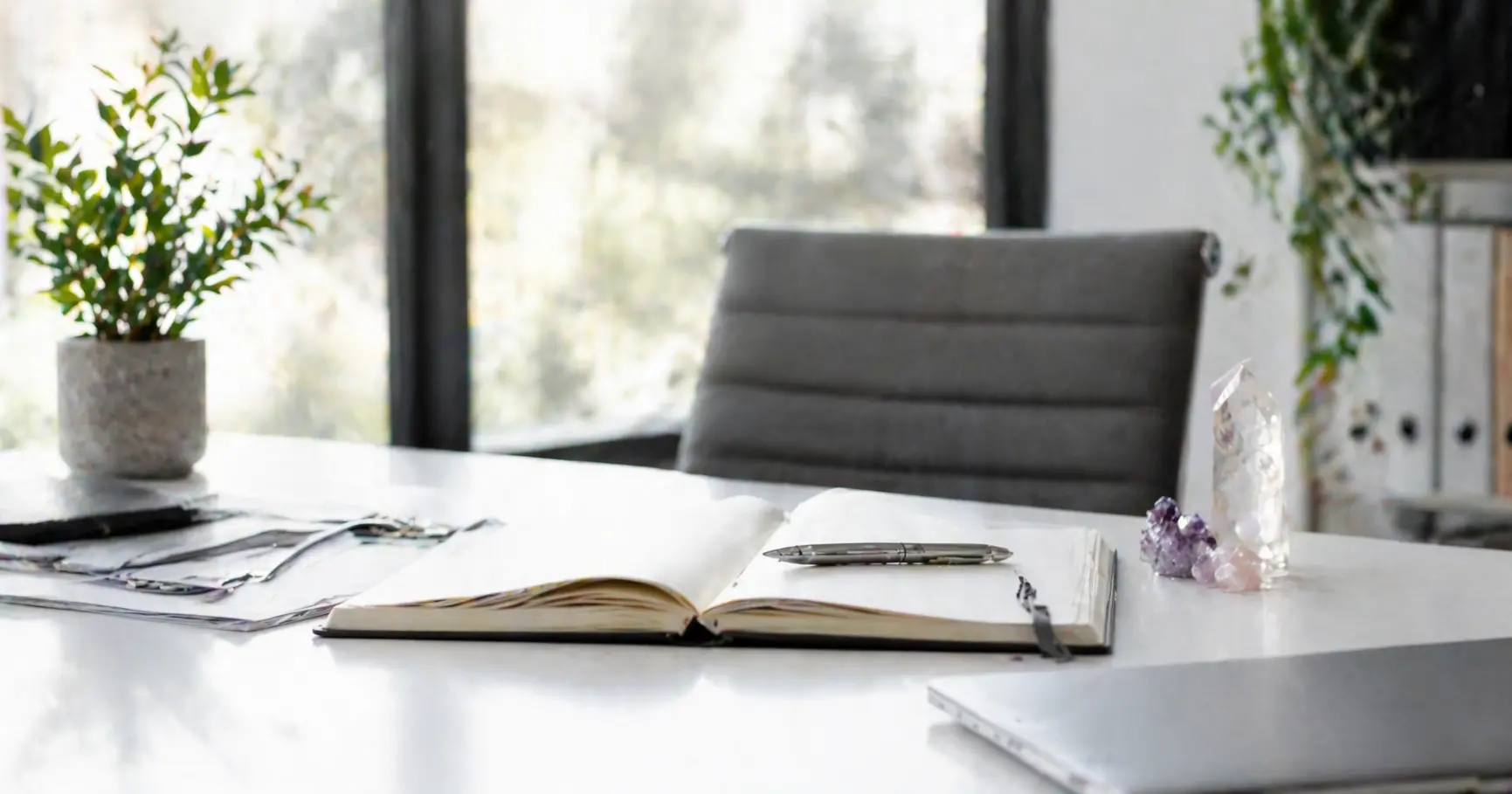 Bureau épuré avec cahier ouvert, stylo, plante verte et cristaux symbolisant le cadre professionnel et éthique des soins énergétiques