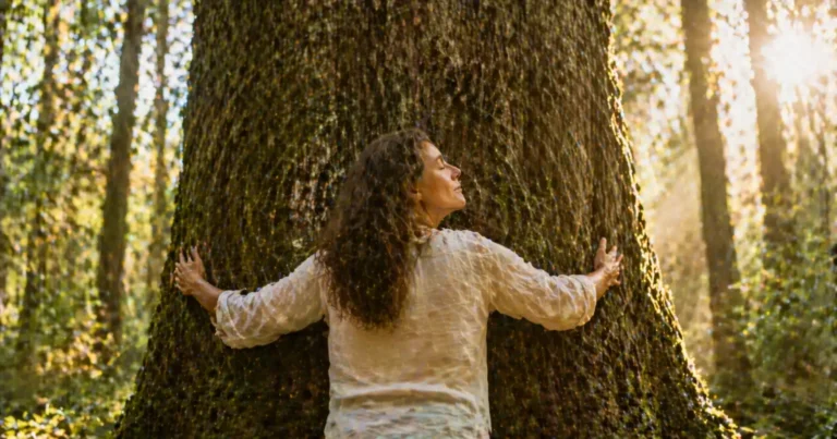 Personne adulte au milieu d'une forêt, paumes posées sur un arbre majestueux dans une pratique de sylvothérapie
