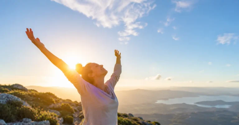 Personne faisant une pause régénératrice à l'extérieur, bras étirés vers le ciel et visage tourné vers la lumière