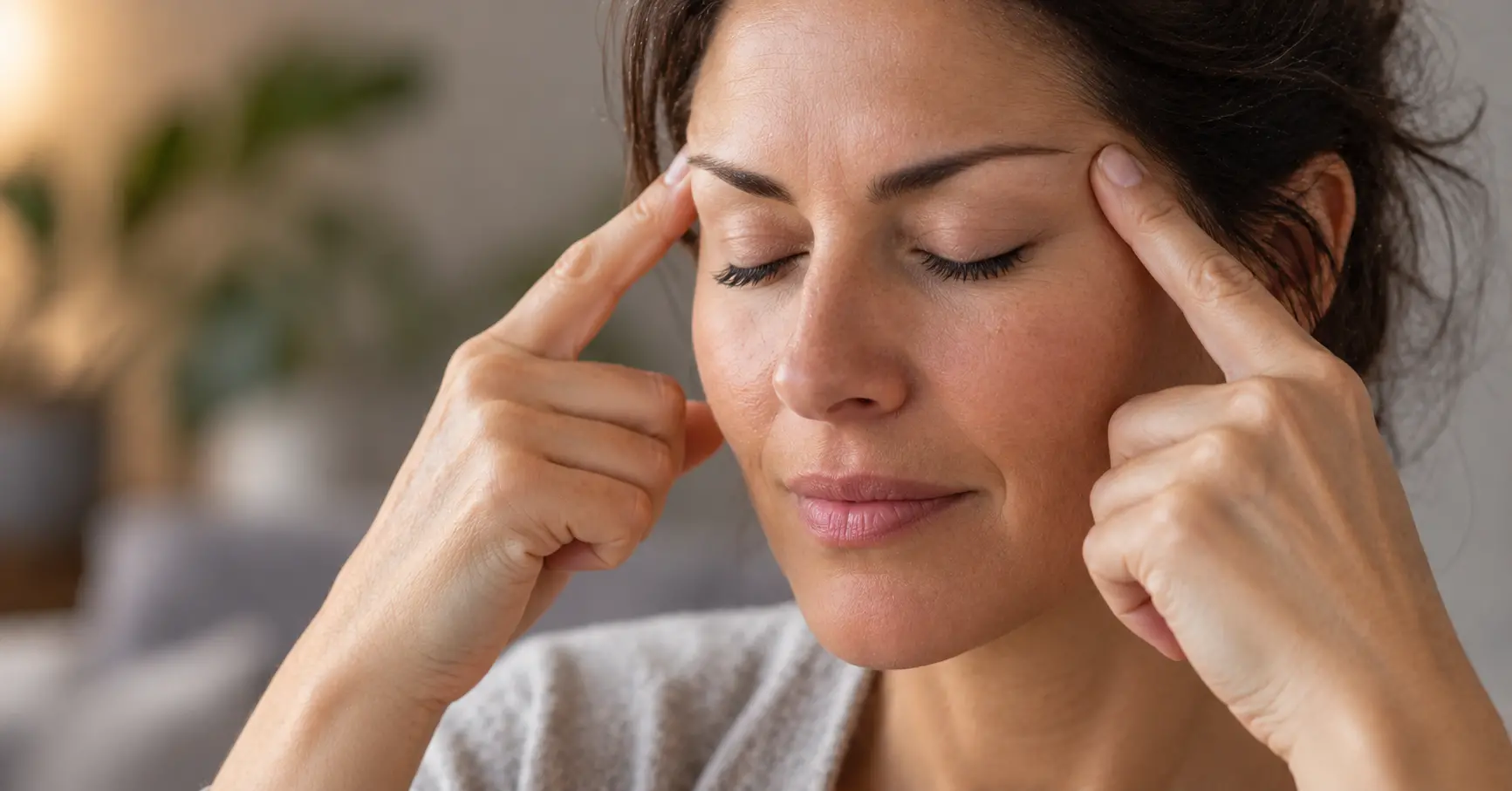 Femme aux yeux fermés exerçant une pression douce des deux index sur ses tempes, à l'emplacement du point Taiyang, pour soulager un mal de tête